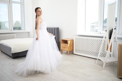 Photo of Dreams come true. Woman wearing beautiful wedding dress looking at herself in mirror indoors