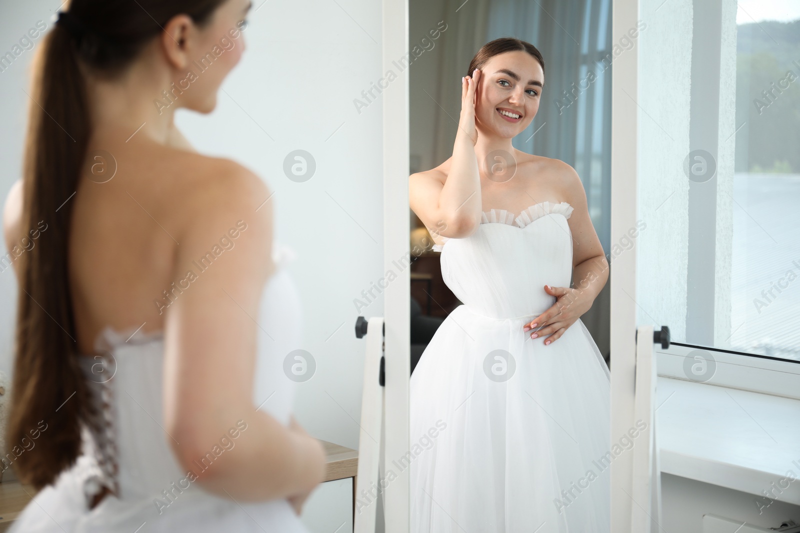 Dreams come true. Woman wearing beautiful wedding dress looking at herself in mirror indoors Photo of Dreams come true. Woman wearing beautiful wedding dress looking at herself in mirror indoors