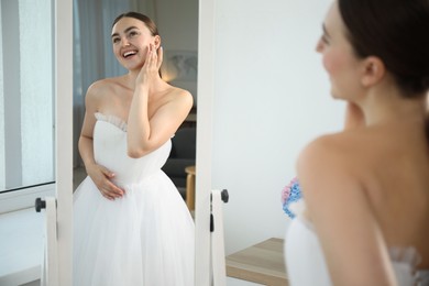 Photo of Dreams come true. Woman wearing beautiful wedding dress looking at herself in mirror indoors