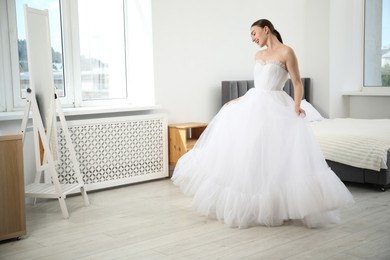 Photo of Dreams come true. Woman wearing beautiful wedding dress looking at herself in mirror indoors