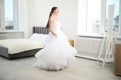 Photo of Dreams come true. Woman wearing beautiful wedding dress looking at herself in mirror indoors