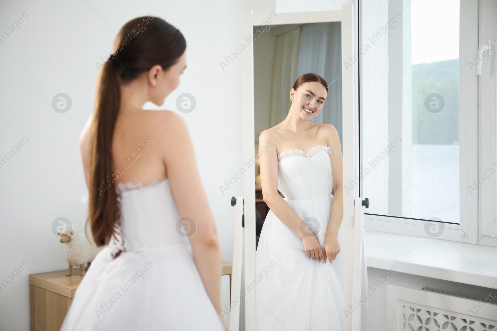 Dreams come true. Woman wearing beautiful wedding dress looking at herself in mirror indoors Photo of Dreams come true. Woman wearing beautiful wedding dress looking at herself in mirror indoors