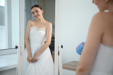 Photo of Dreams come true. Woman wearing beautiful wedding dress looking at herself in mirror indoors