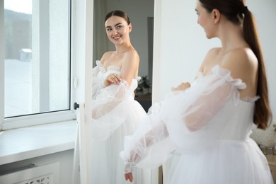 Photo of Dreams come true. Woman wearing beautiful wedding dress looking at herself in mirror indoors