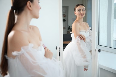 Photo of Dreams come true. Woman wearing beautiful wedding dress looking at herself in mirror indoors