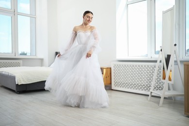 Photo of Dreams come true. Woman wearing beautiful wedding dress looking at herself in mirror indoors