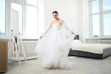 Photo of Dreams come true. Woman wearing beautiful wedding dress looking at herself in mirror indoors