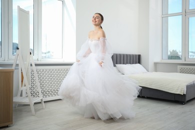 Photo of Dreams come true. Woman wearing beautiful wedding dress looking at herself in mirror indoors
