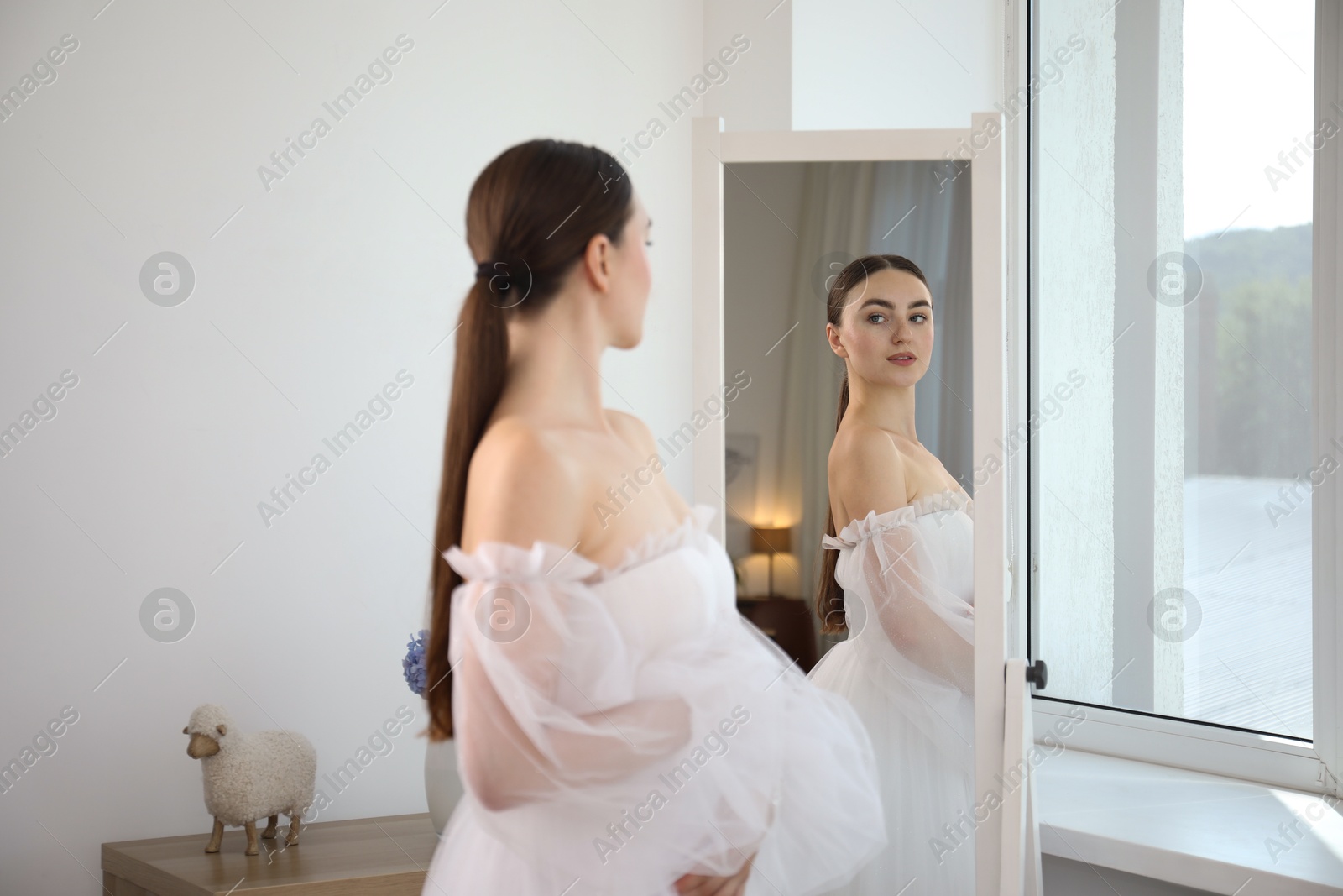 Dreams come true. Woman wearing beautiful wedding dress looking at herself in mirror indoors Photo of Dreams come true. Woman wearing beautiful wedding dress looking at herself in mirror indoors