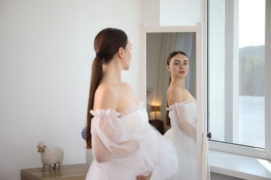 Photo of Dreams come true. Woman wearing beautiful wedding dress looking at herself in mirror indoors