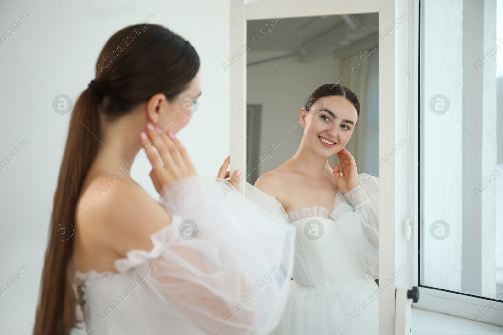 Dreams come true. Woman wearing beautiful wedding dress looking at herself in mirror indoors Photo of Dreams come true. Woman wearing beautiful wedding dress looking at herself in mirror indoors
