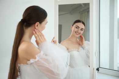 Photo of Dreams come true. Woman wearing beautiful wedding dress looking at herself in mirror indoors