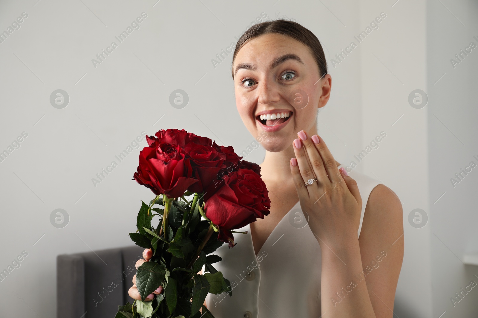 Photo of Dreams come true. Surprised woman with engagement ring and beautiful bouquet indoors