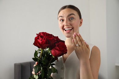 Photo of Dreams come true. Surprised woman with engagement ring and beautiful bouquet indoors