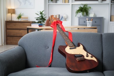 Photo of Dreams come true. Guitar with bow on sofa at home, space for text