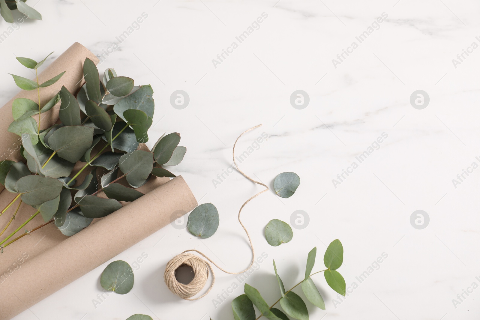 Photo of Florist. Eucalyptus branches, thread and wrapping paper on white marble table, flat lay. Space for text