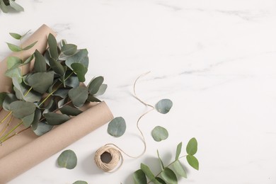 Photo of Florist. Eucalyptus branches, thread and wrapping paper on white marble table, flat lay. Space for text