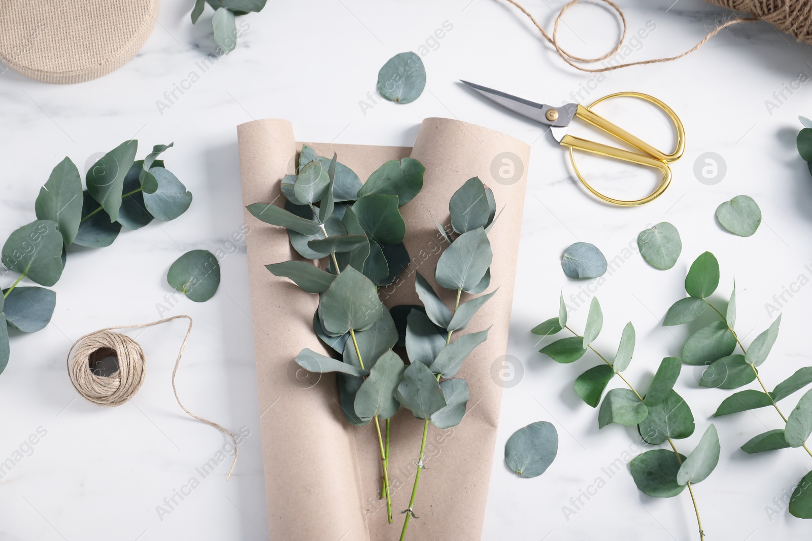 Florist. Eucalyptus branches, thread, scissors and wrapping paper on white marble table, flat lay Photo of Florist. Eucalyptus branches, thread, scissors and wrapping paper on white marble table, flat lay