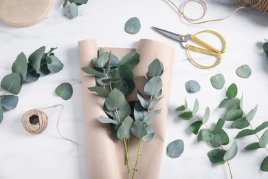 Photo of Florist. Eucalyptus branches, thread, scissors and wrapping paper on white marble table, flat lay