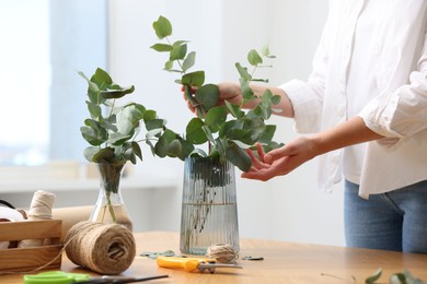 Photo of Florist making beautiful bouquet of eucalyptus branches at wooden table in flower shop, closeup