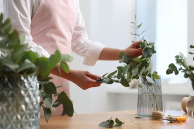 Photo of Florist making beautiful bouquet of eucalyptus branches at wooden table in flower shop, closeup