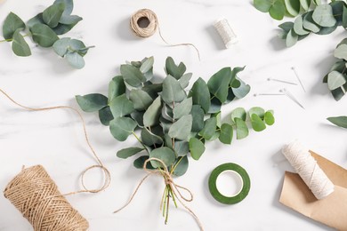 Photo of Florist. Eucalyptus branches, threads, ribbon, pins and wrapping paper on white marble table, flat lay