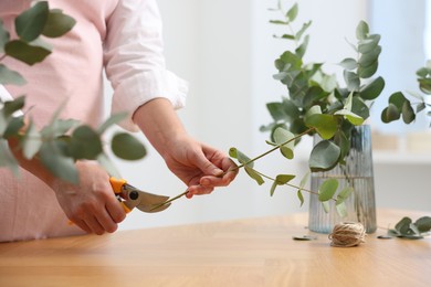 Photo of Florist making beautiful bouquet of eucalyptus branches at wooden table in flower shop, closeup