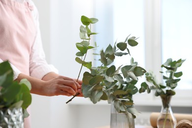 Photo of Florist making beautiful bouquet of eucalyptus branches in flower shop, closeup