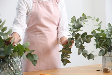 Photo of Florist making beautiful bouquet of eucalyptus branches at wooden table in flower shop, closeup