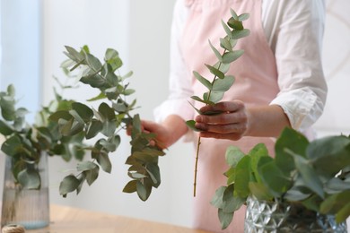 Photo of Florist making beautiful bouquet of eucalyptus branches at table in flower shop, closeup