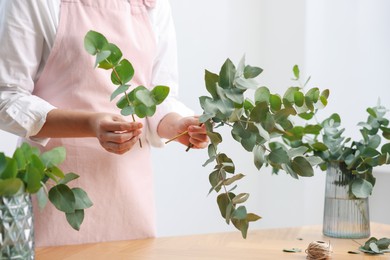 Photo of Florist making beautiful bouquet of eucalyptus branches at wooden table in flower shop, closeup