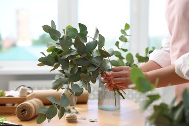 Photo of Florist making beautiful bouquet of eucalyptus branches at wooden table in flower shop, closeup
