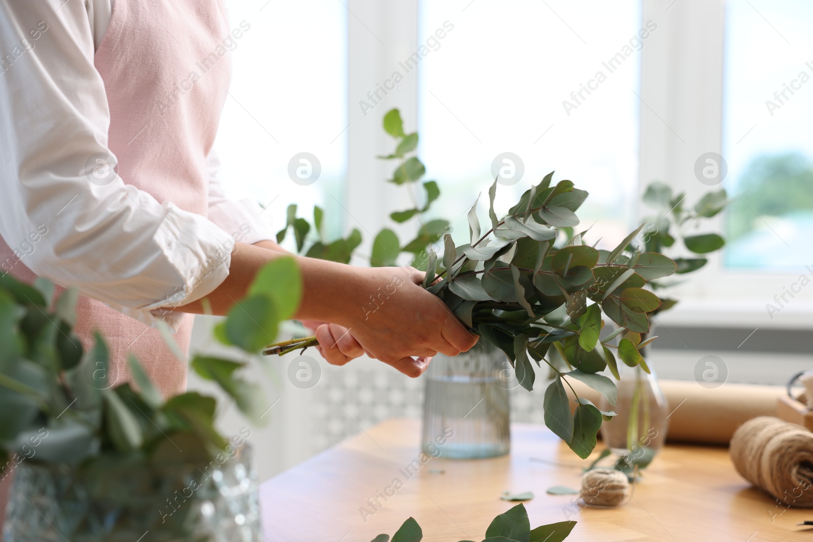 Photo of Florist making beautiful bouquet of eucalyptus branches at wooden table in flower shop, closeup