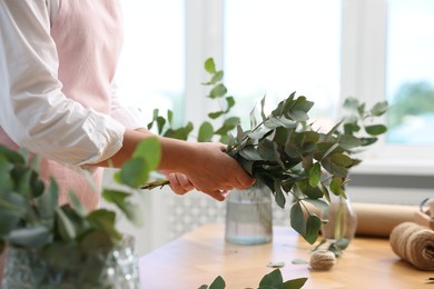 Photo of Florist making beautiful bouquet of eucalyptus branches at wooden table in flower shop, closeup