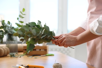 Photo of Florist making beautiful bouquet of eucalyptus branches at wooden table in flower shop, closeup