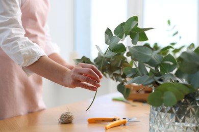 Photo of Florist making beautiful bouquet of eucalyptus branches at wooden table in flower shop, closeup