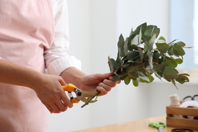 Photo of Florist making beautiful bouquet of eucalyptus branches in flower shop, closeup