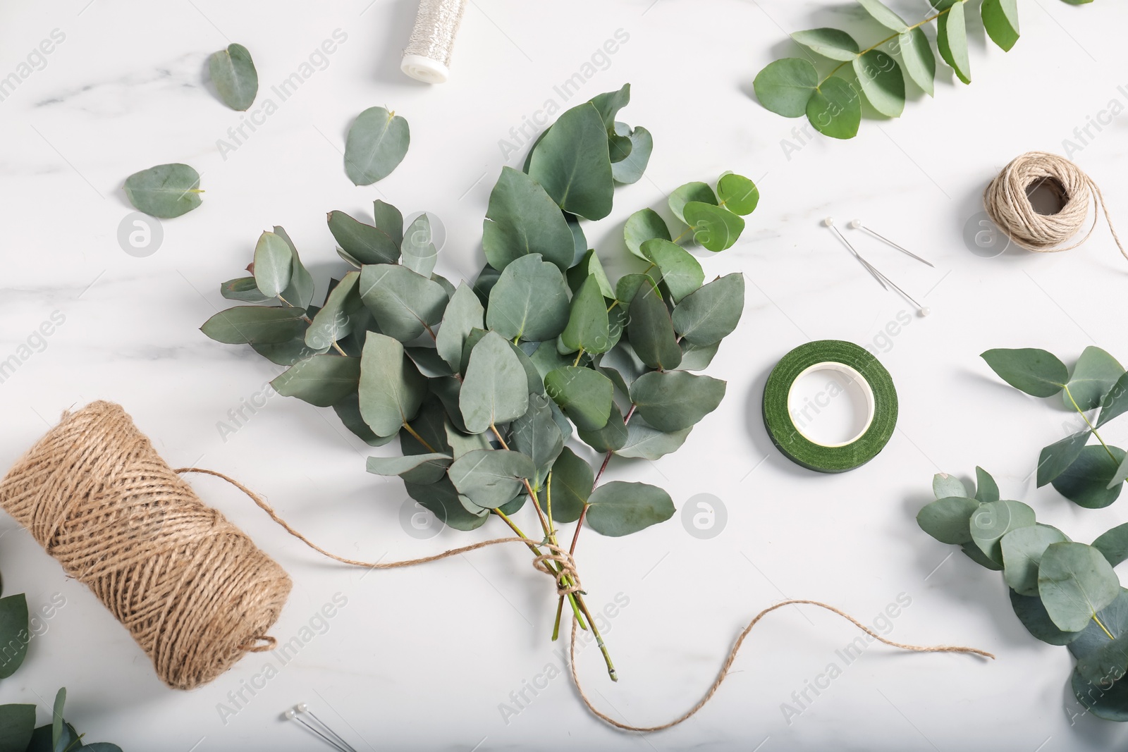 Florist. Eucalyptus branches, threads, ribbon and pins on white marble table, flat lay Photo of Florist. Eucalyptus branches, threads, ribbon and pins on white marble table, flat lay