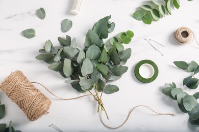 Photo of Florist. Eucalyptus branches, threads, ribbon and pins on white marble table, flat lay