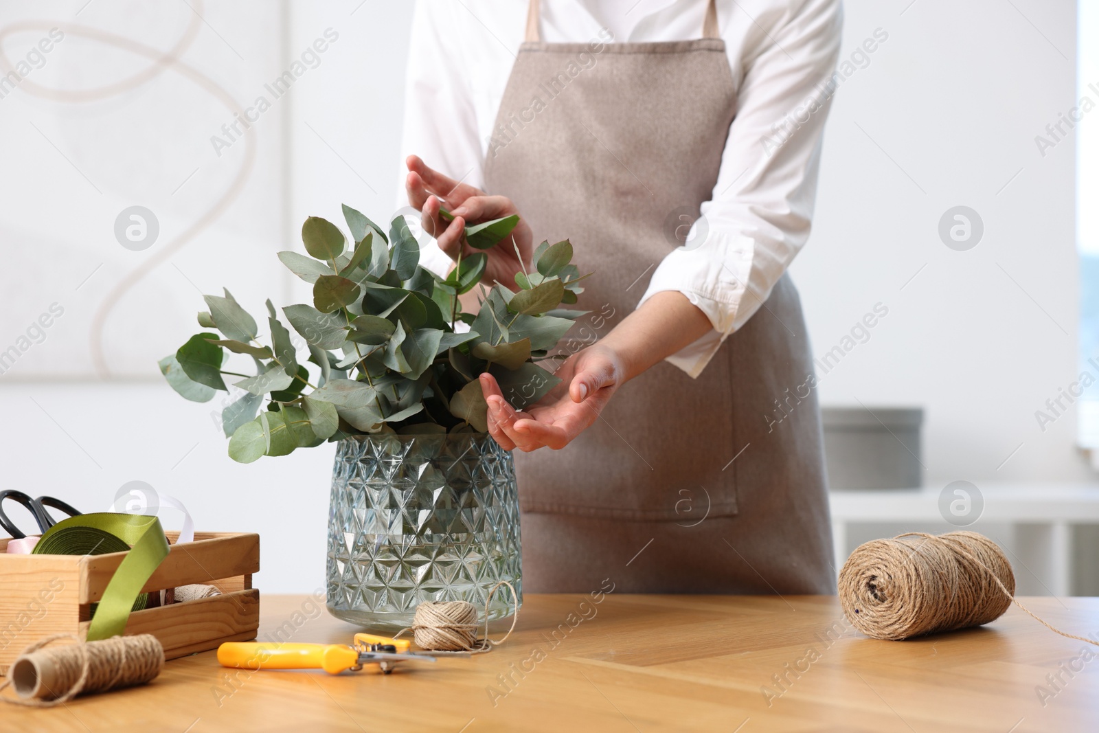 Photo of Florist making beautiful bouquet of eucalyptus branches at wooden table in flower shop, closeup