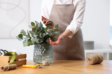 Photo of Florist making beautiful bouquet of eucalyptus branches at wooden table in flower shop, closeup