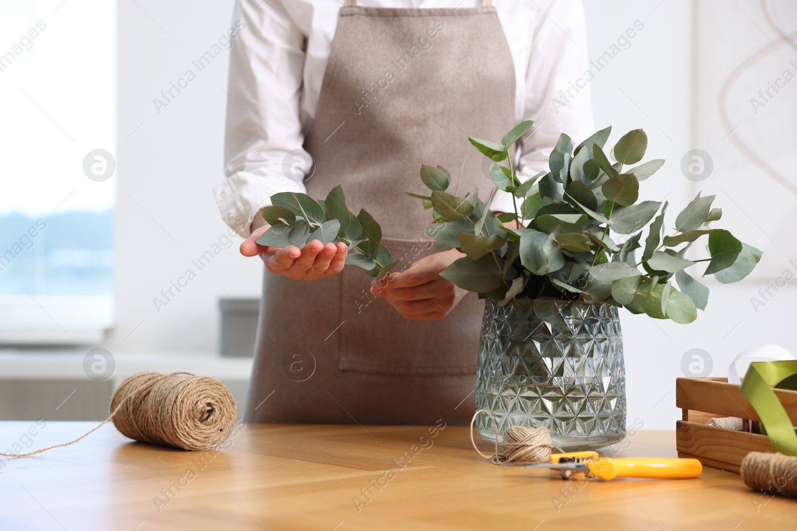 Florist making beautiful bouquet of eucalyptus branches at wooden table in flower shop, closeup Photo of Florist making beautiful bouquet of eucalyptus branches at wooden table in flower shop, closeup