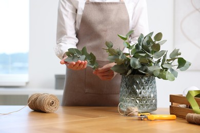 Photo of Florist making beautiful bouquet of eucalyptus branches at wooden table in flower shop, closeup