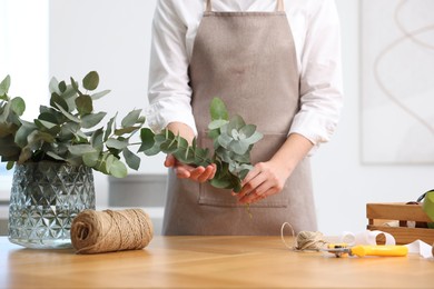 Photo of Florist making beautiful bouquet of eucalyptus branches at wooden table in flower shop, closeup