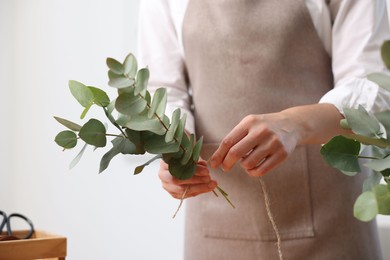 Photo of Florist making beautiful bouquet of eucalyptus branches in flower shop, closeup