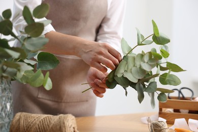 Photo of Florist making beautiful bouquet of eucalyptus branches at wooden table in flower shop, closeup