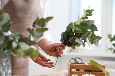 Photo of Florist making beautiful bouquet of eucalyptus branches in flower shop, closeup