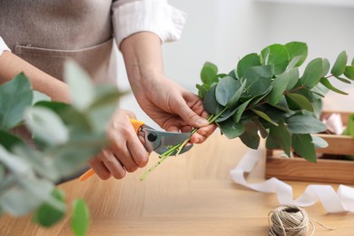 Photo of Florist making beautiful bouquet of eucalyptus branches at wooden table in flower shop, closeup