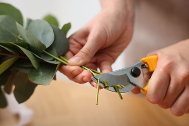 Photo of Florist making beautiful bouquet of eucalyptus branches at table in flower shop, closeup