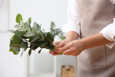 Photo of Florist making beautiful bouquet of eucalyptus branches in flower shop, closeup